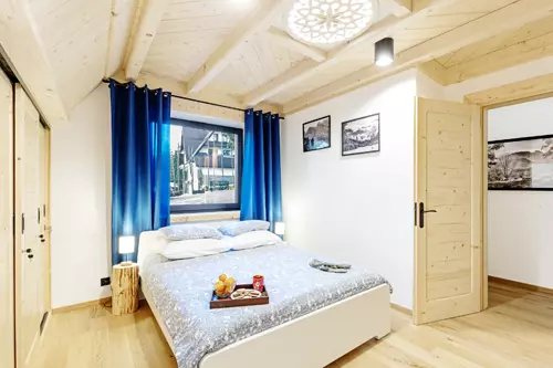 Sypialnie Willa Uroczysko. Widok na łóżko oraz okno za którym stoi budynek.